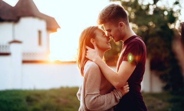 Çekici bir çift arka planda beyaz bir binayla öpüşüyor yaz günbatımı gezisinde poz veriyorlar.