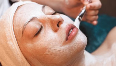 Kapalı gözlü, spa merkezinde beyaz bir yüz maskesi takan beyaz bir kadının yakın plan fotoğrafını çek.