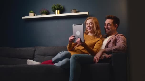 Nettes Paar sitzt mit Tablet auf der Couch und lächelt beim gemeinsamen Entspannen — Stockvideo