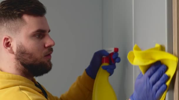 Ο γενειοφόρος άνδρας εργάζεται στο σπίτι καθαρίζοντας το σπίτι χρησιμοποιώντας ένα μαντηλάκι με αντιβακτηριακό σπρέι. — Αρχείο Βίντεο