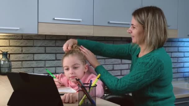 Mãe branca está consertando o cabelo da filha enquanto ela está tendo aulas on-line usando um laptop — Vídeo de Stock