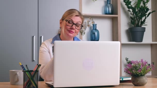 Blonde Oberärztin spricht mit dem Patienten per Laptop im Büro — Stockvideo
