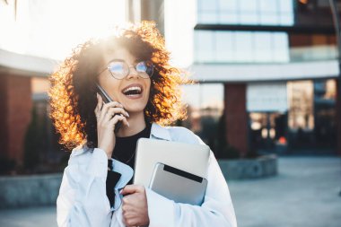 Tabletle poz verirken telefonda konuşan kıvırcık saçlı ve gözlüklü çekici girişimci.