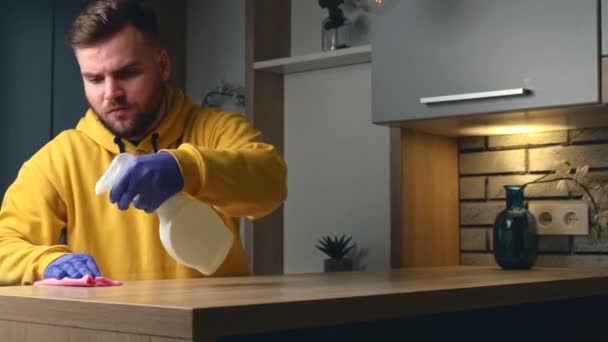 Baard blanke man in een gele trui is het reinigen van de tafel met antibacteriële spray — Stockvideo