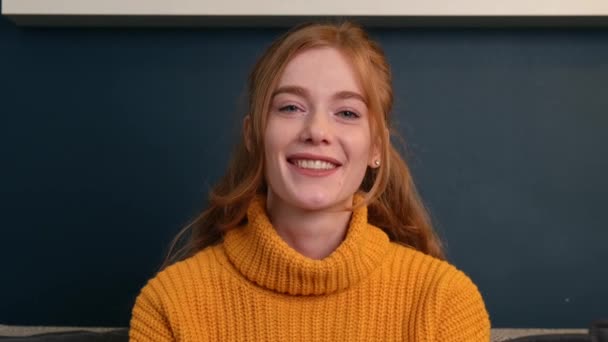 Ginger woman with freckles is greeting somebody on camera talking with a blackboard on background — Αρχείο Βίντεο