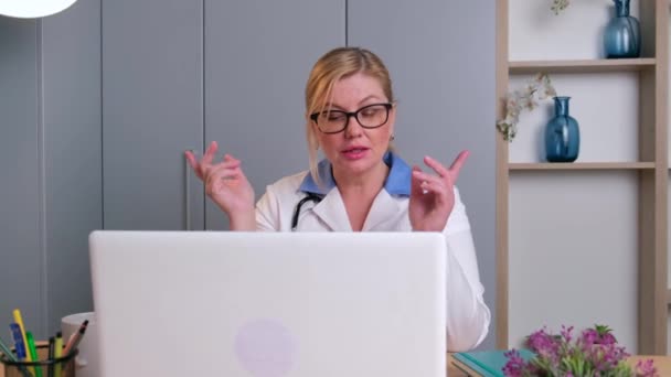 선임 금발 의사가 온라인으로 환자와 사무실에서 노트북으로 통화중입니다 — 비디오