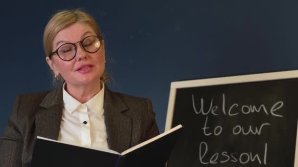 Κοντινό βίντεο από μια ηλικιωμένη γυναίκα με γυαλιά που μιλάει κοντά στον πίνακα εξηγεί το θέμα κατά τη διάρκεια του online μαθήματος — Αρχείο Βίντεο