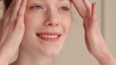 Kızıl saçlı bir kadının çilli yüzüne krem sürerken ve gülümserken yakın plan fotoğrafını çek.