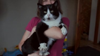 Caucasian woman is holding a big black cat in hands smiling at camera