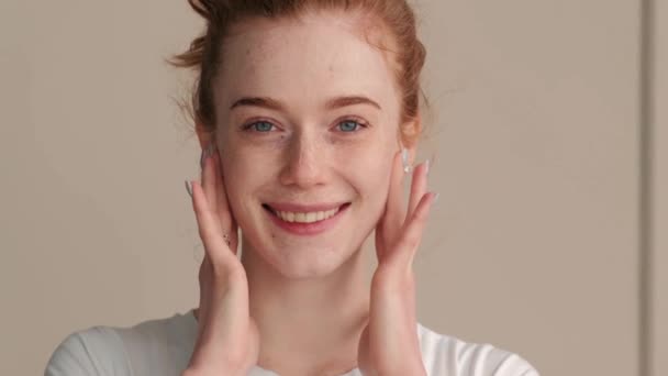 Mujer adorable con pecas y el pelo rojo sonríe a la cámara mientras se aplica crema en la cara — Vídeos de Stock