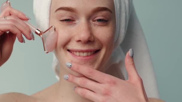 Freckled woman with ginger hair is massaging her face with a derma roller smiling at camera — Vídeo de Stock