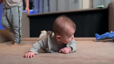 Sevimli yeni doğmuş bebek kanepede yatarken ağabeyi onun etrafında oynuyor.