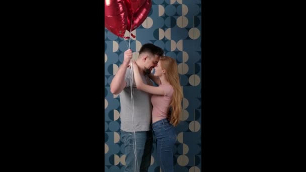 Encantador casal estão escondidos atrás de balões de ar vermelho beijando uns aos outros — Vídeo de Stock