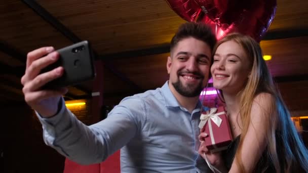 Kaukasisk par kysser efter mand gav hende en gave og røde balloner gør en selfie – Stock-video