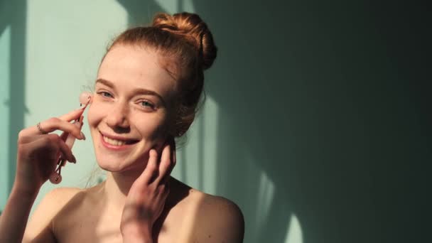 Caucasian ginger woman with freckles is using a derma roller on her face smiling with bare shoulders — Stock Video