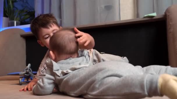 Маленький белый мальчик играет со своим новорожденным братом, трогает его голову и улыбается. — стоковое видео