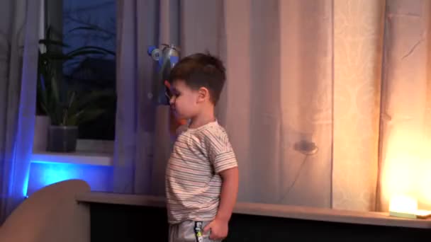 Kaukasische jongen spelen met een vliegtuig laat in de avond in zijn kamer in de buurt van het raam met een lamp — Stockvideo