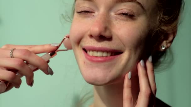 Roodharige blanke vrouw met sproeten masseren haar gezicht met een derma roller glimlachen op camera op een groene studio muur — Stockvideo