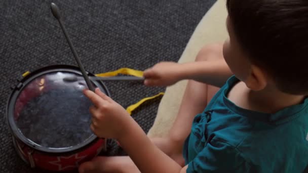 Caucasian boy is playing a drum on the floor sitting on a pillow and simulating a song — Stock Video