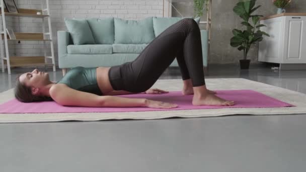 Biała sportowa kobieta wykonuje ćwiczenia fitness w domu na podłodze w odzieży sportowej — Wideo stockowe