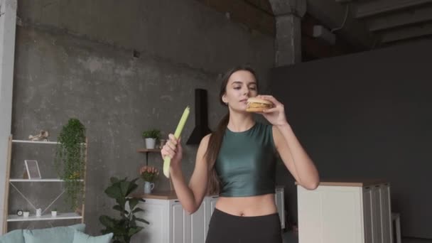 Kavkazská přemýšlivá žena se rozhoduje mezi zdravým jídlem a nezdravým jídlem, které drží hamburger a pórek doma — Stock video