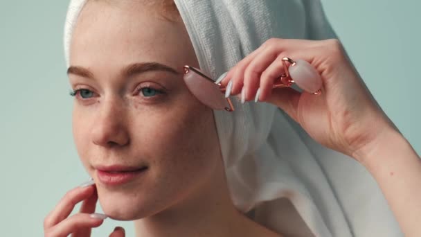 Relaxing freckled woman is massaging her face with a derma roller wearing a white towel on head — Stock Video