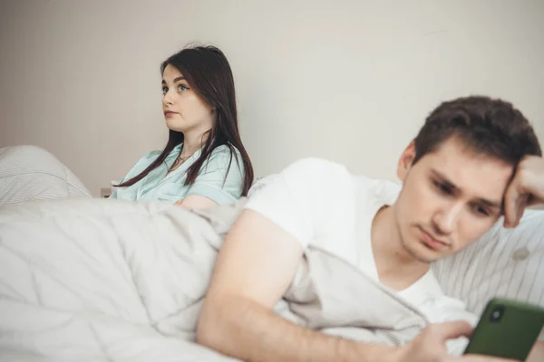 Femme caucasienne bouleversée est triste parce que son mari est à la recherche dans le mobile tout en étant couché dans le lit — Photo