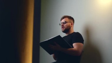 Sakallı adam elinde bir kitap tutarken ve kameraya doğru konuşurken çevrimiçi bir stüdyo duvarında video eğitimi alıyor.