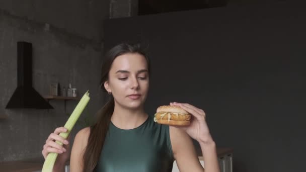 Caucasian sporty woman is making her choice between healthy and junk food eating a burger — Stock Video