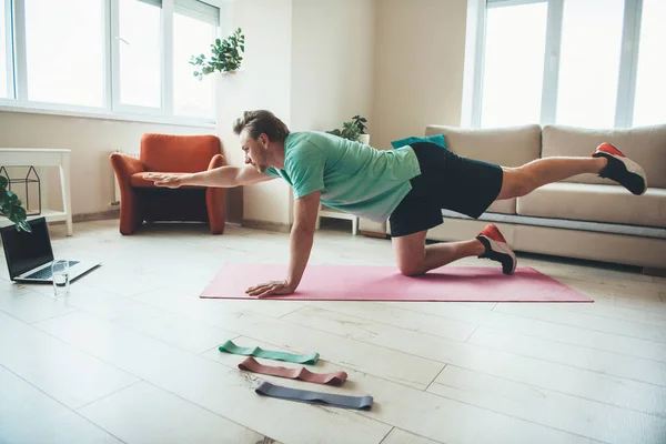 Блондин мужчина растягивается во время фитнес-упражнений дома с помощью ноутбука на полу — стоковое фото