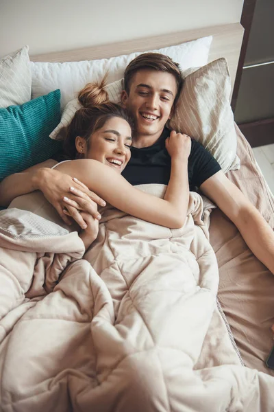 Vista superior de una pareja caucásica acostada en la cama cubierta con una manta sonriendo y abrazando —  Fotos de Stock