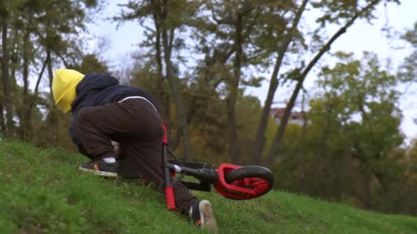 Kaukasische jongen vallen en dragen van de fiets op de heuvel tijdens het spelen in een groen park — Stockvideo