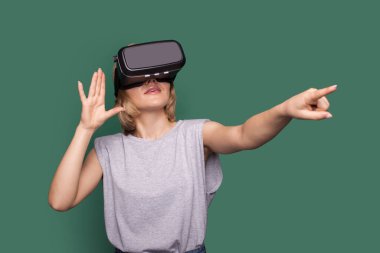 Sarışın kadın yeşil bir stüdyo duvarında artırılmış gerçeklik kulaklığı kullanırken bir şeye dokunuyor.