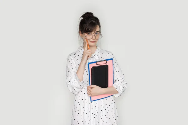 Estudiante de moda está sosteniendo carpetas y usando gafas mientras posa en una pared blanca en la cámara —  Fotos de Stock