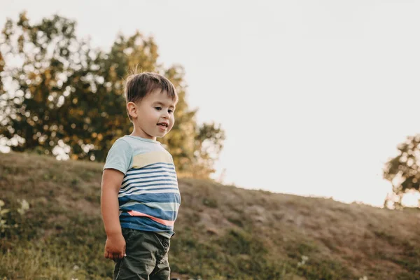 Menino pequeno está sorrindo enquanto joga em um campo em uma colina durante uma caminhada de verão — Fotografia de Stock