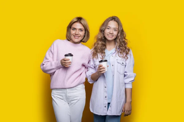 Schwestern mit blonden Haaren trinken gemeinsam einen Kaffee an einer gelben Studiowand und lächeln in die Kamera — Stockfoto