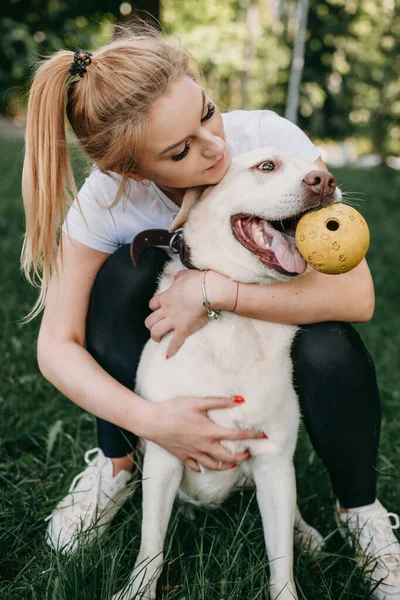 Fehér nő és labradora játszik egy parkban a füvön egy játéklabdával. — Stock Fotó