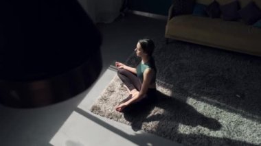 Beyaz bir kadın yoga seansı sırasında evde yerde meditasyon yapıyor.