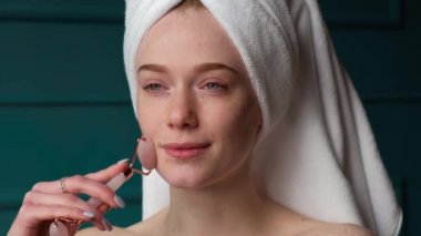 Çilli beyaz kadın evinde banyo yaptıktan sonra yüzüne deri silindiri ile masaj yapıyor.