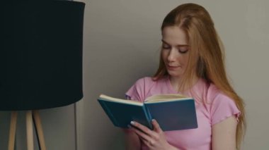 Çilli kızıl kadın kitap okuyor ve evde bir şeyler not ediyor.