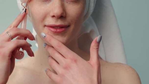 Ruda kobieta z piegami uśmiecha się podczas masażu twarzy kamiennym wałkiem do skóry — Wideo stockowe