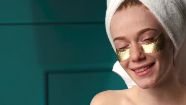 Ginger woman with freckles is smiling at camera after taking a bath wearing golden eye patches — Stock Video