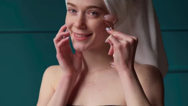 Belle femme taches de rousseur se masse le visage avec un rouleau derma souriant à la caméra après le bain — Video