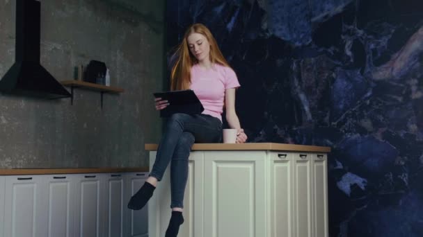 Adorable young ginger woman with freckles having a coffee break in the kitchen sitting on the table — Stock Video