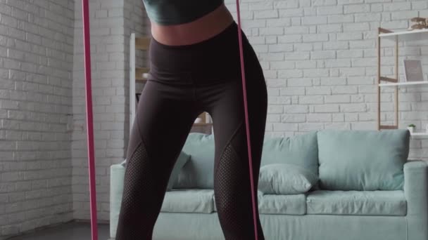 Sporty woman is using elastic bands having fitness session at home — Stock video
