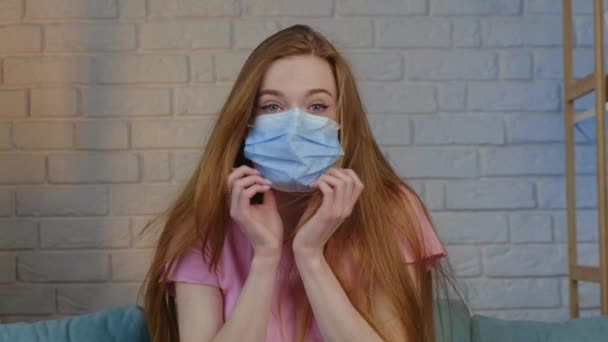 Caucasian woman with freckles and res hair is trying to wear a medical mask at home — Stock Video