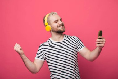 Sarışın, sakallı, sarı saçlı, kırmızı stüdyo duvarında dans eden kulaklıkla müzik dinleyen bir adam.