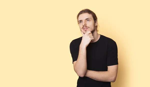 Homem atencioso com barba e cabelos longos está anunciando algo em uma parede amarela com espaço livre — Fotografia de Stock