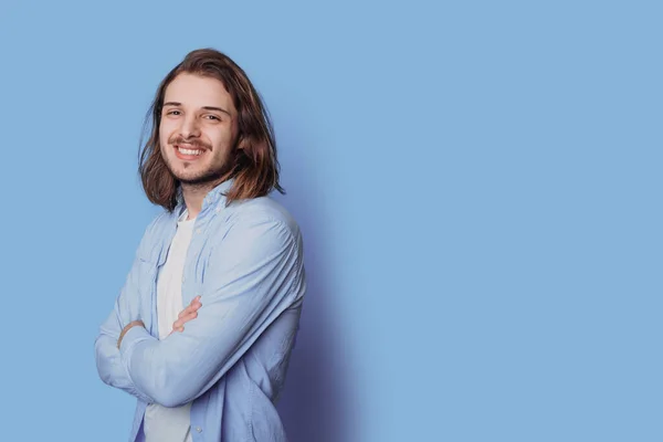 Homem caucasiano com barba está sorrindo para a câmera em uma parede de estúdio azul com espaço livre posando com as mãos cruzadas — Fotografia de Stock