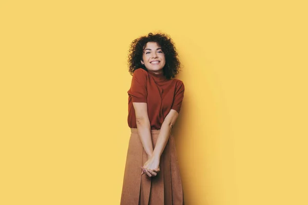 Donna caucasica con i capelli ricci sorride alla macchina fotografica su un muro giallo studio indossa un abito alla moda — Foto Stock
